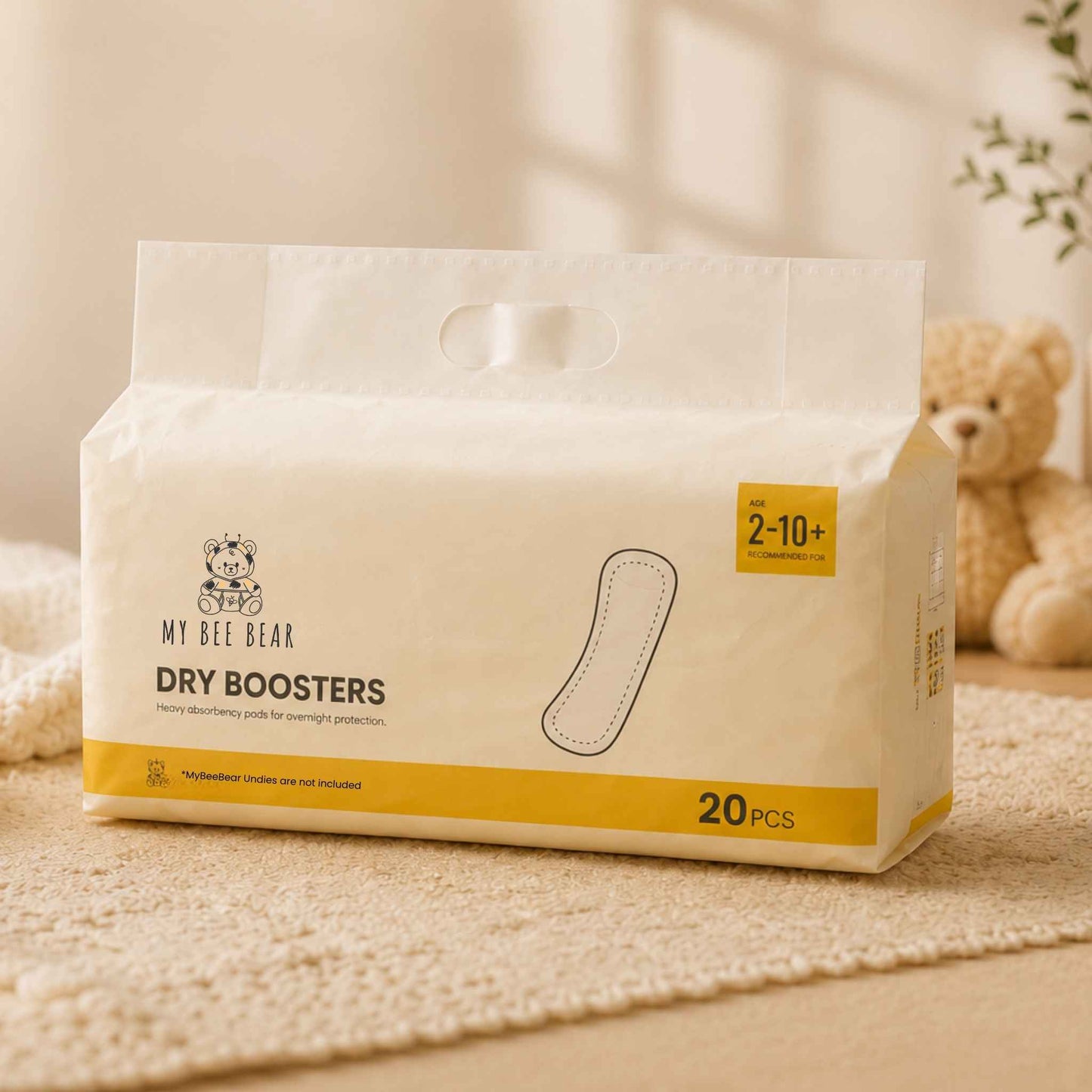 A package of My Bee Bear Dry Boosters hand towels, featuring a warm off-white design with yellow accents and a small teddy bear logo, set on a textured beige rug with a soft-focus teddy bear in the background.