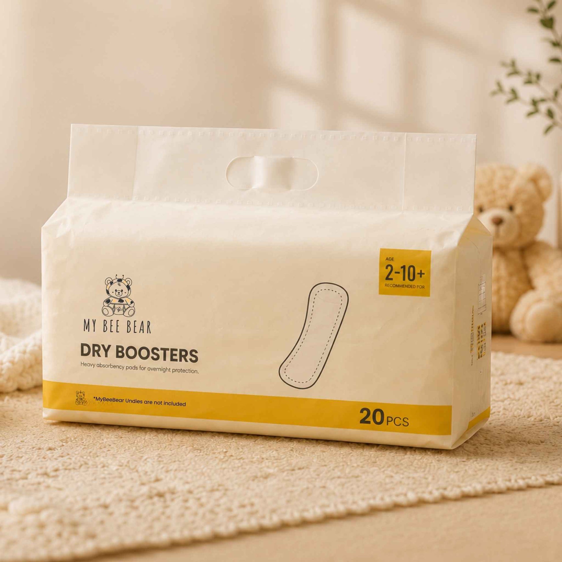 A package of My Bee Bear Dry Boosters hand towels, featuring a warm off-white design with yellow accents and a small teddy bear logo, set on a textured beige rug with a soft-focus teddy bear in the background.