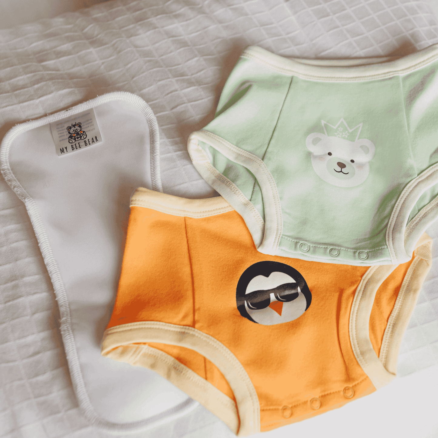 Two pairs of children's underwear, one green with a bear design and one orange with a cloud design, on a textured surface.