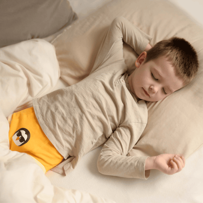 Child sleeping in a bed with beige bedding and yellow bedwetting pants