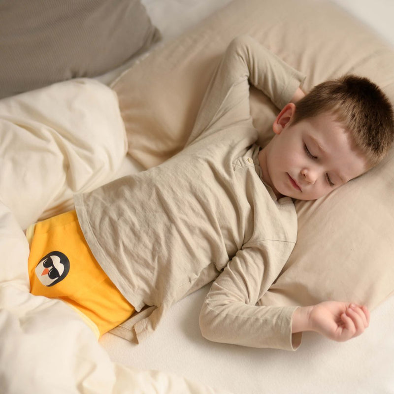 Child sleeping in a bed with a yellow penguin-patterned diaper.