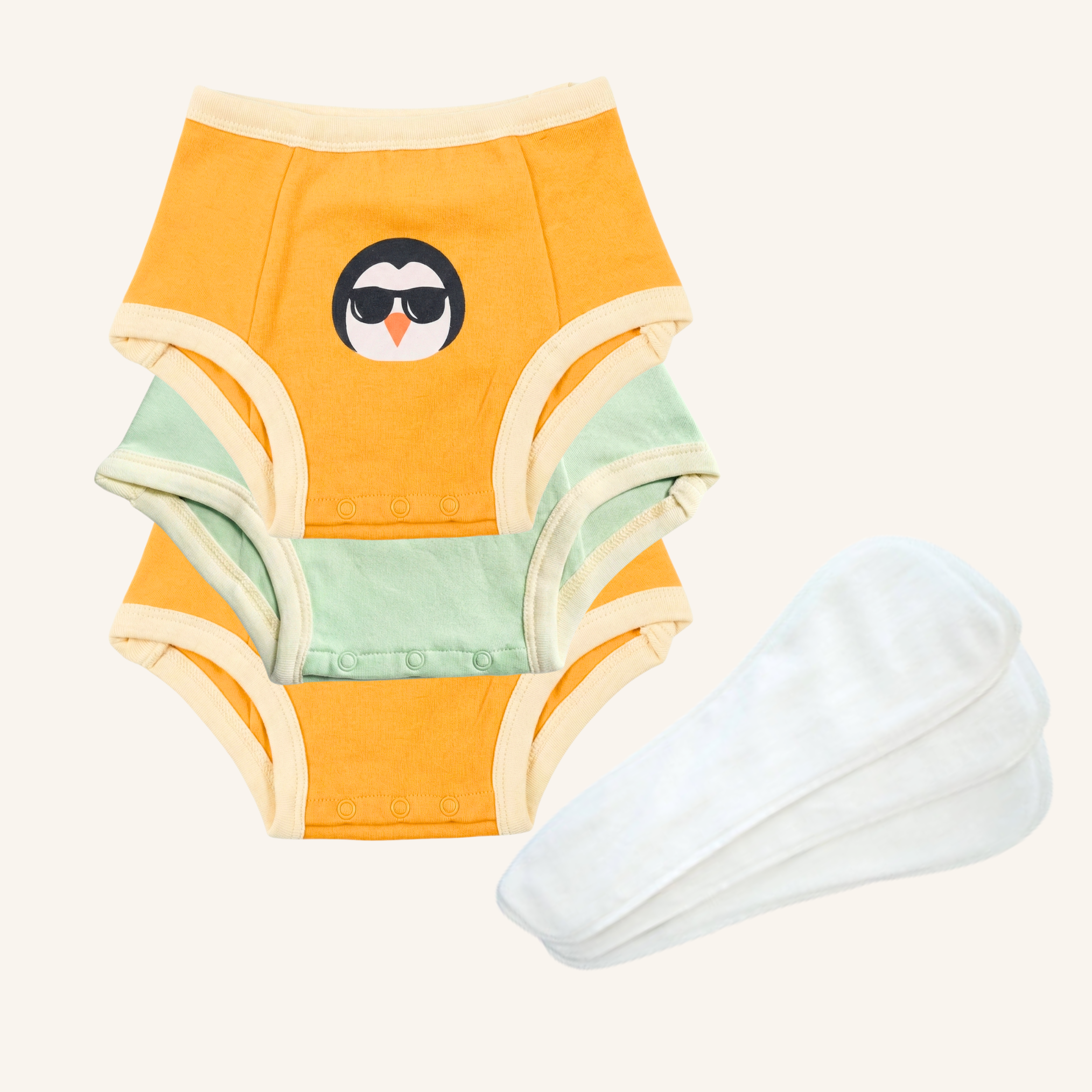 Orange baby nighttime underwear with penguin design and white pants on a white background