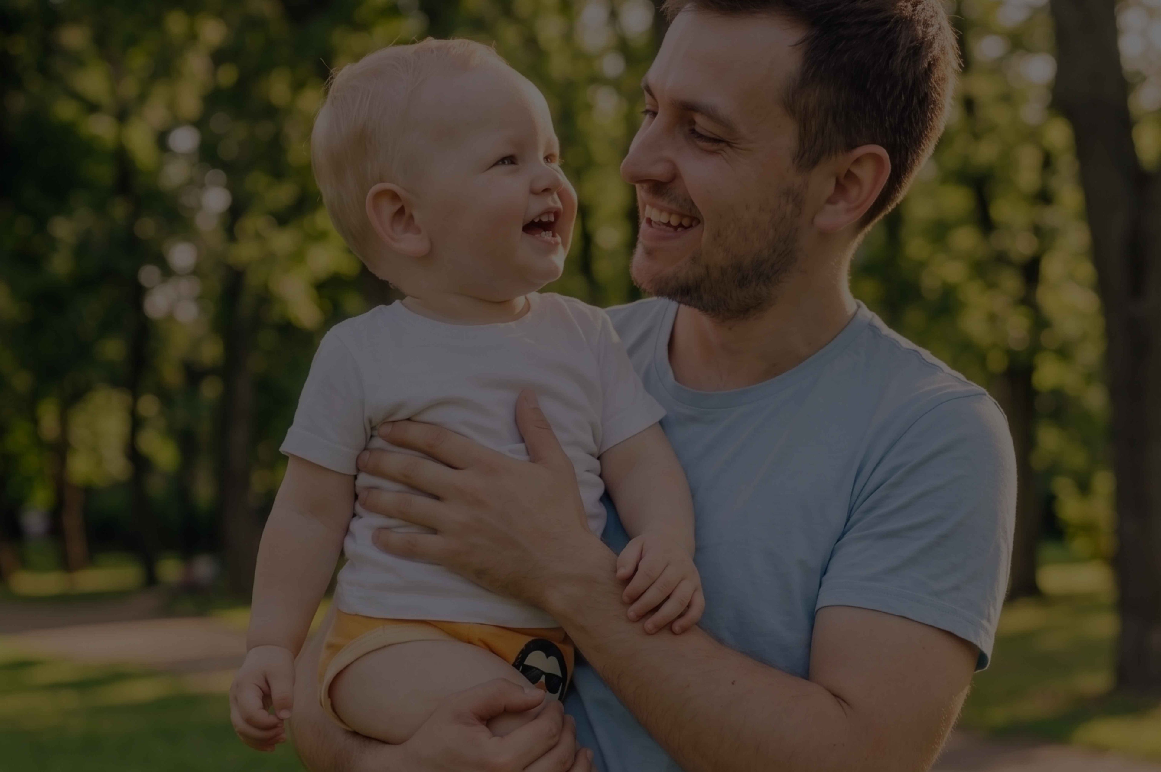 Man holding a baby in a park with trees in the background