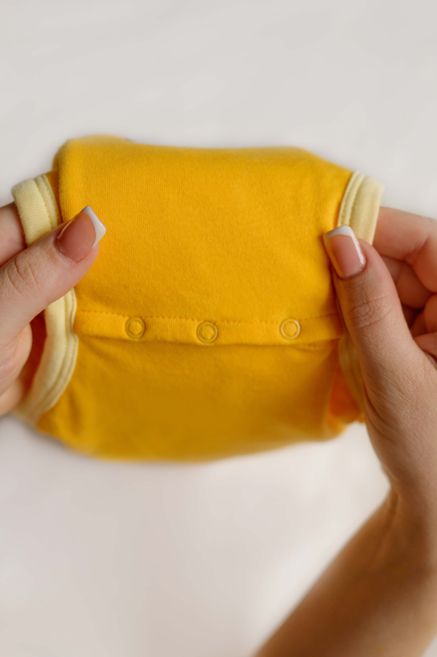 Yellow baby outfit held by hands on a light background